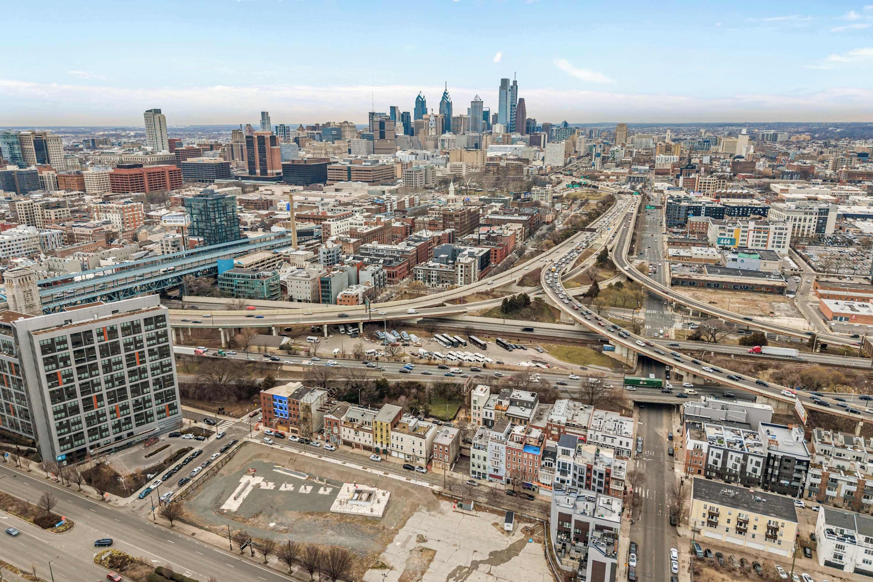 An aerial view of a cityscape with a mix of modern and older buildings, a complex highway system, and a clear sky.