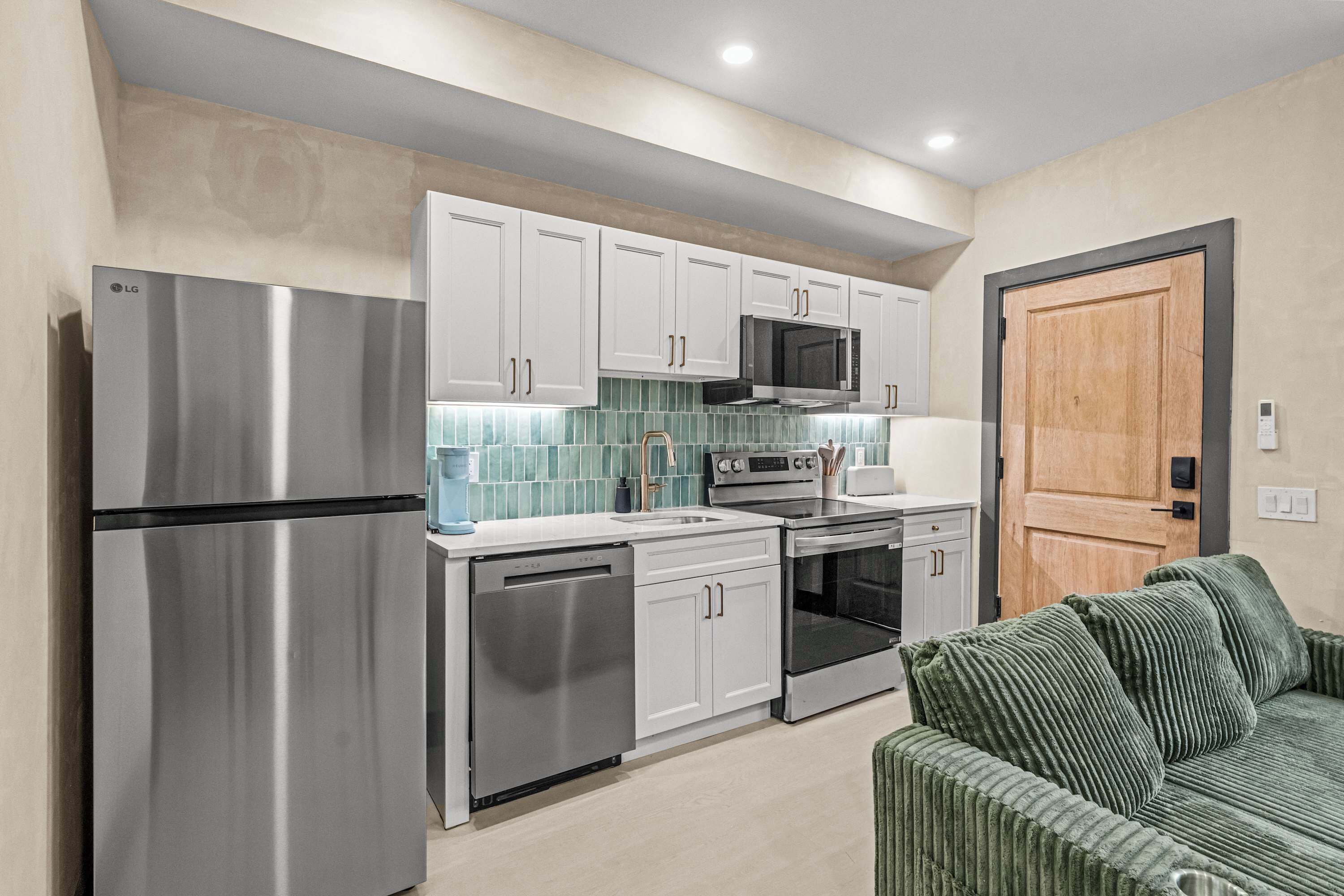 A modern kitchen with stainless steel appliances, white cabinets, and a green sofa.