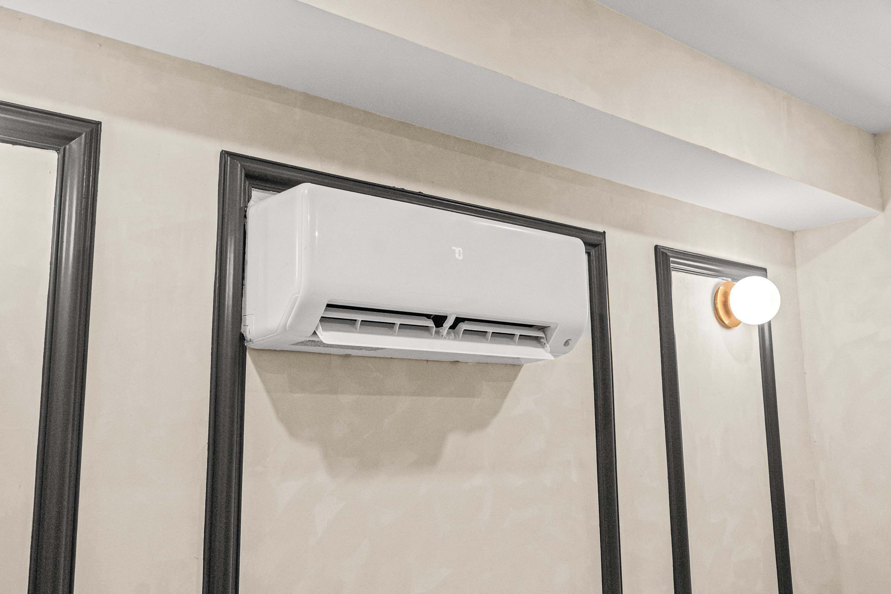 Un equipo de aire acondicionado instalado en la pared de una habitación con una pared lisa y una puerta con un aplique de luz redondo.