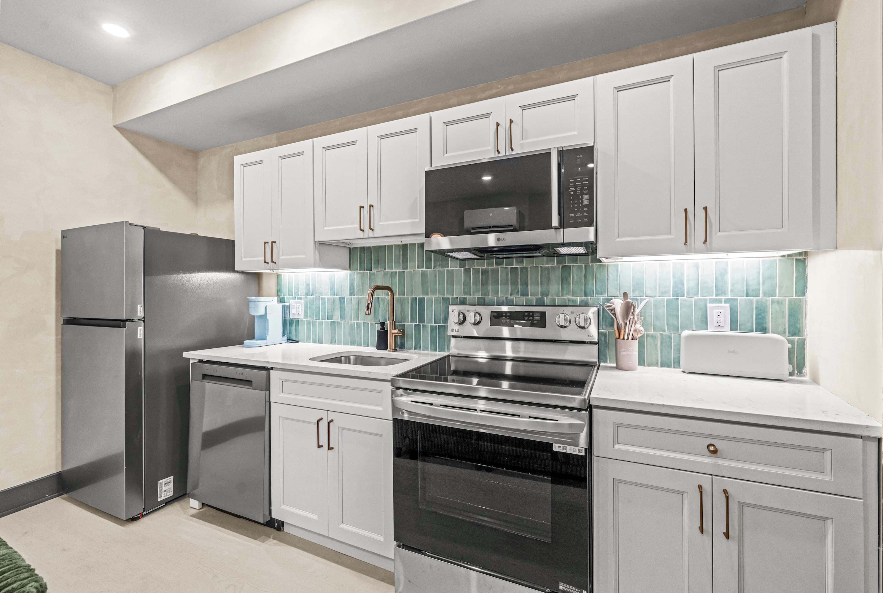 A modern kitchen with stainless steel appliances, white cabinetry, and a green tiled backsplash.