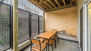 Un patio techado con una mesa y sillas de madera, una malla y piso de concreto.