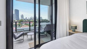 Ein Hotelzimmer mit Balkon, einem Bett, einem Sessel, einem kleinen Tisch und einem Nachttisch mit Lampe.