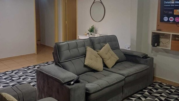Olohuone, jossa on harmaa sohva, kuviollinen matto ja seinälle asennettu televisio.