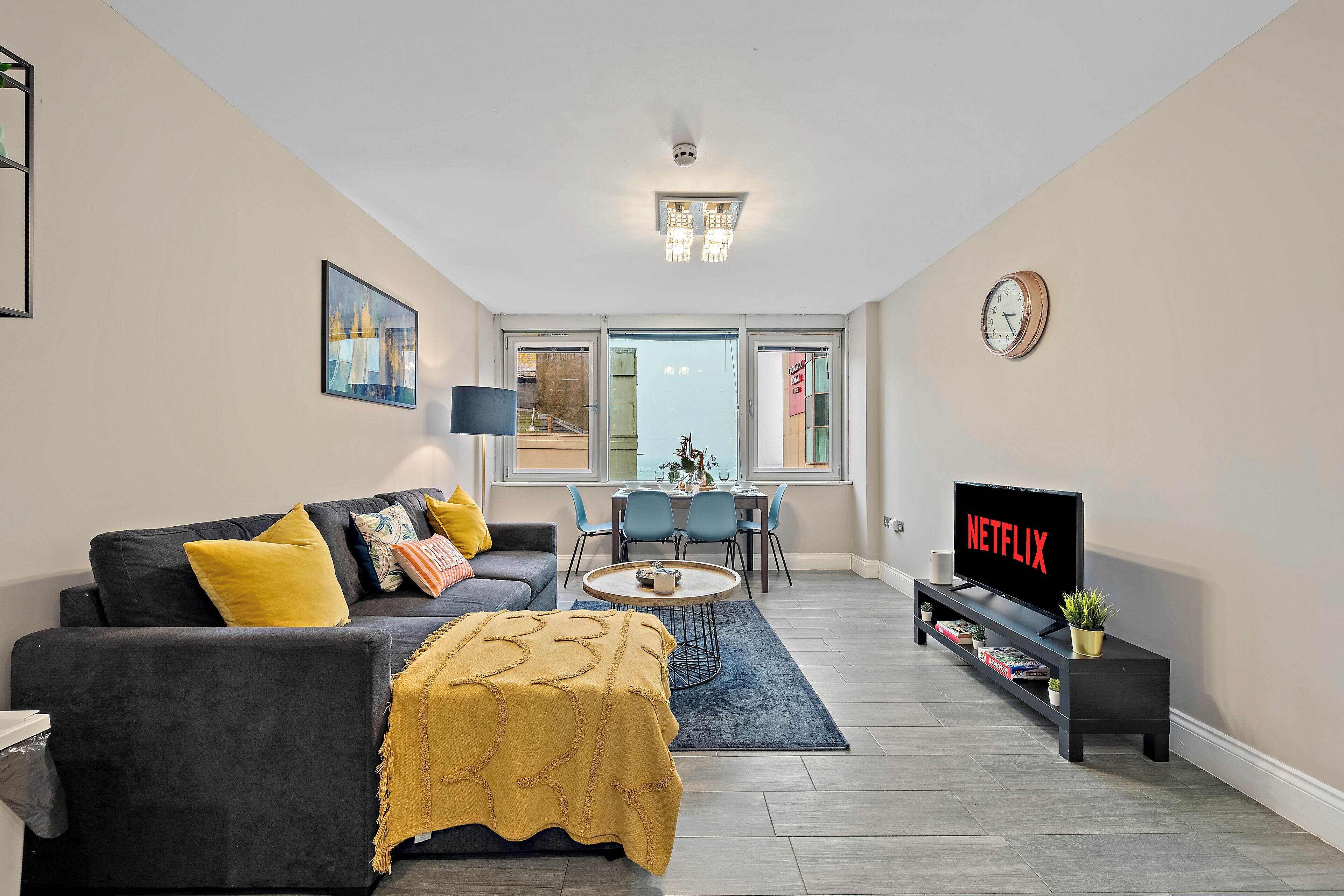 Una sala de estar moderna con un sofá oscuro, un cojín amarillo y un televisor que muestra 'NETFLIX'.