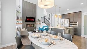 Ein moderner Essbereich mit einem Marmortisch, schwarzen Stühlen und einem Fernseher, der 'NETFLIX' anzeigt.