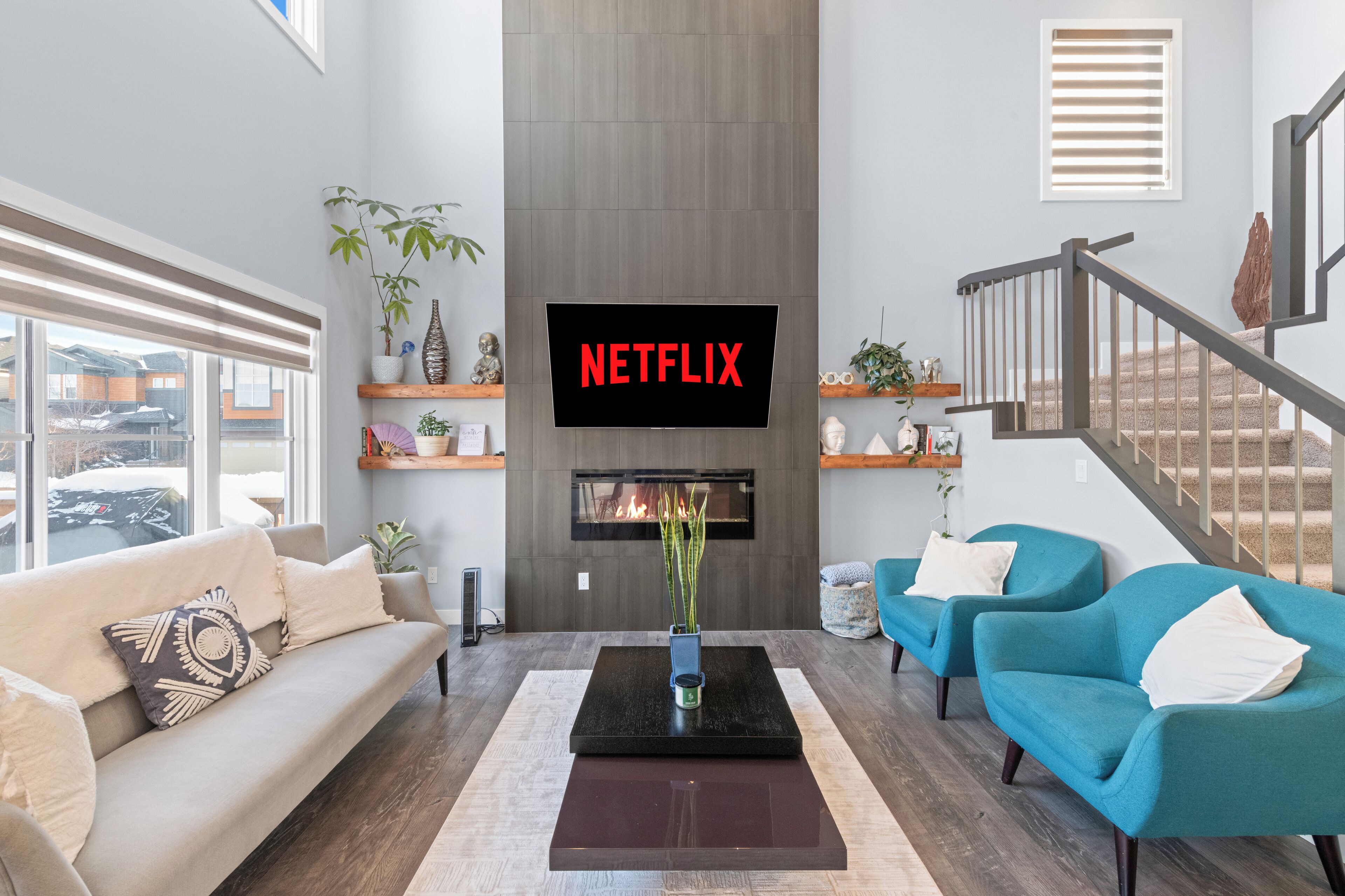 Ein modernes Wohnzimmer mit Kamin, einem Wand-Fernseher mit 'NETFLIX' und einer Treppe.