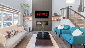 Ein modernes Wohnzimmer mit Kamin, einem Wand-Fernseher mit 'NETFLIX' und einer Treppe.