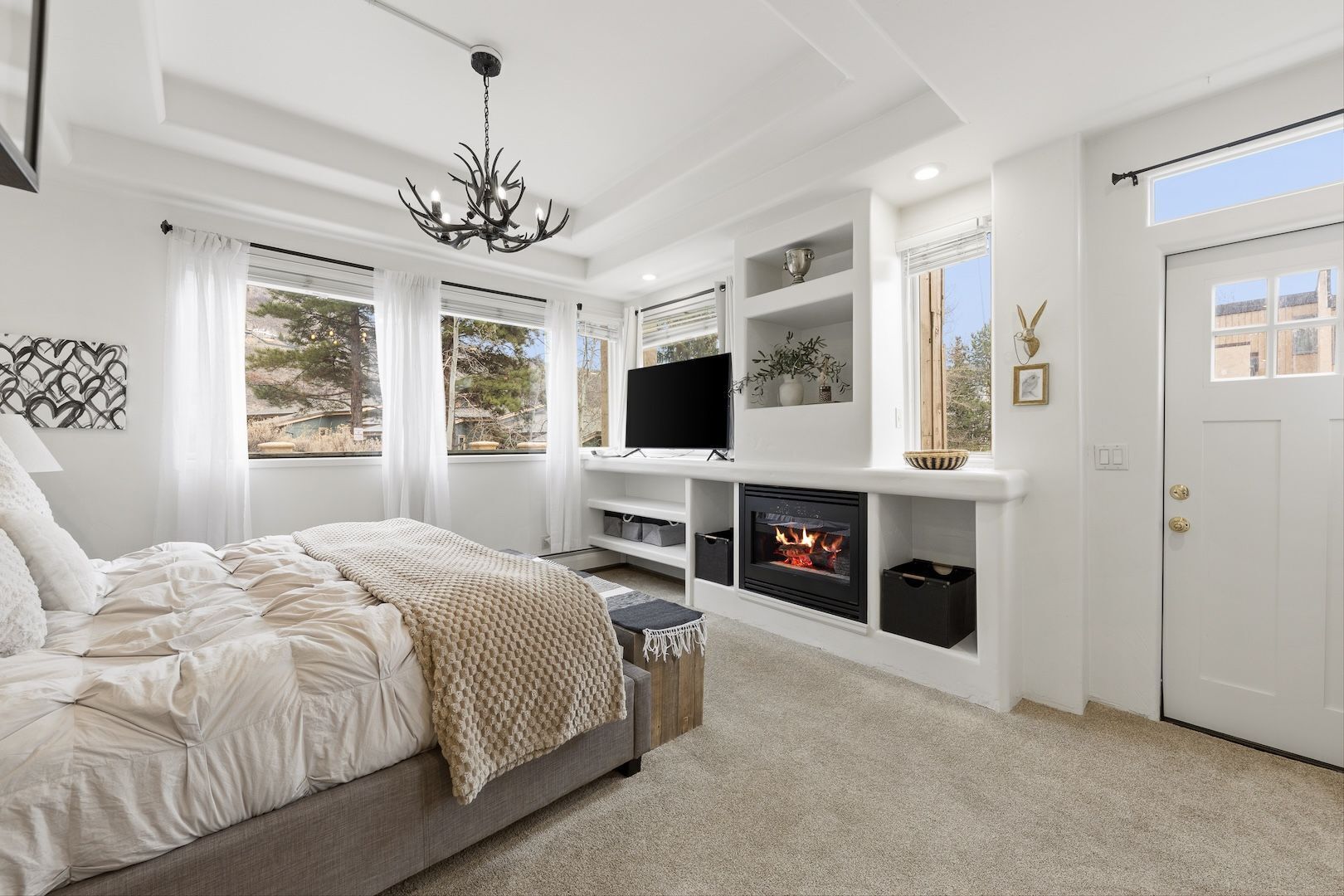 A bedroom with a bed, a fireplace, a television, and a window with curtains.
