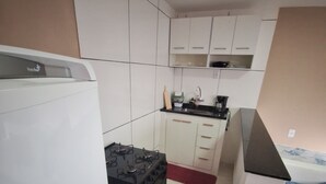 A compact kitchen with white cabinets, a black stove, and a red rug.