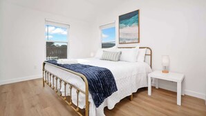A bedroom with a bed, two windows, a ceiling fan, a nightstand, and a painting. - Beachside Oasis I Walk to the Beach I Ocean view I (Jacksonville Beach)