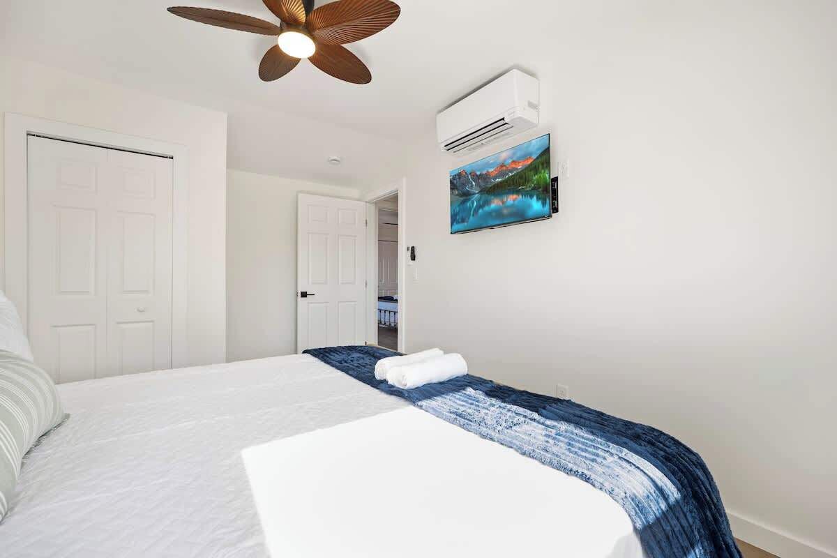 Een hotelkamer met een bed, een plafondventilator, een airconditioningsysteem en een schilderij aan de muur.