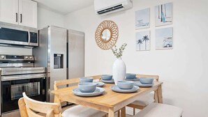 A modern kitchen with stainless steel appliances, a wooden dining table with blue bowls, and a white vase with greenery. - Beachside Oasis I Walk to the Beach I Ocean view I (Jacksonville Beach)