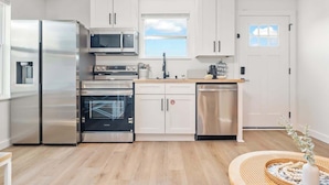 A modern kitchen with stainless steel appliances, white cabinetry, and a view of the sky through a window. - Beachside Bliss I 1 bedroom + loft I Oceanviews (Jacksonville Beach)