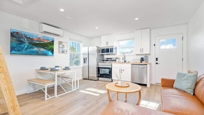A modern kitchen with white cabinets, stainless steel appliances, and a dining area with a wooden table and benches. - Beachside Bliss I 1 bedroom + loft I Oceanviews (Jacksonville Beach)