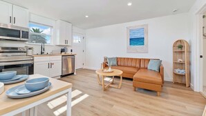 A modern kitchen with white cabinets, a dining table with blue plates, a leather sofa, and a wicker shelf. - Beachside Bliss I 1 bedroom + loft I Oceanviews (Jacksonville Beach)