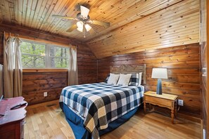 A wooden cabin bedroom with a bed, nightstand, lamp, and a ceiling fan. - Snuggle Inn – Cozy Pet Friendly Forest Cabin with Hot Tub Near Red River Gorge (Stanton)