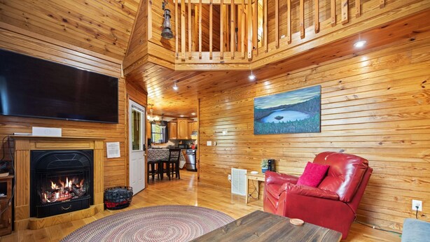 Un interior de madera con chimenea, un sofá de cuero rojo, una zona de comedor y un cuadro en la pared.