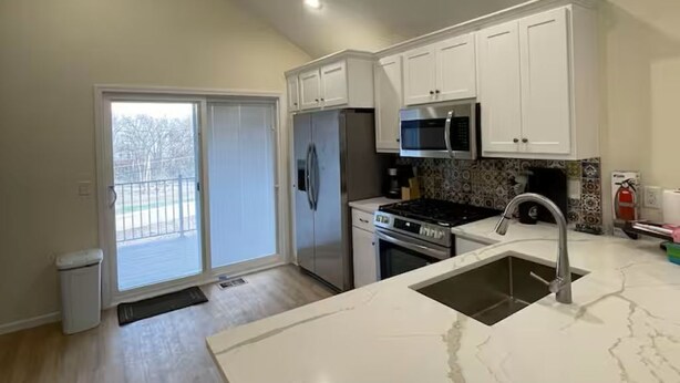 A kitchen with white cabinets, a stainless steel refrigerator, a microwave, and a sink with a marble countertop. - Charming brand new home! Walk to everything! (Atchison)