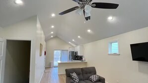 A spacious living area with a ceiling fan, a gray sofa, a wooden coffee table, and a kitchen in the background. - Charming brand new home! Walk to everything! (Atchison)