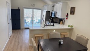 A modern kitchen with white cabinets, a black countertop, and a dining area with a dark table and chairs. - Charming brand new home! Walk to everything! (Atchison)