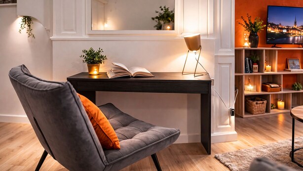 A modern living room with a grey upholstered armchair, a dark wooden side table, a floor lamp, a bookshelf, and a television displaying a cityscape. - Grand T2 Cosy -Rouen historic center near Hôtel de Ville - L'Hauss'Rouennais (Rouen)
