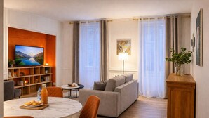 A modern living room with a sofa, a dining table with chairs, a TV, a bookshelf, and a lamp. - Grand T2 Cosy -Rouen historic center near Hôtel de Ville - L'Hauss'Rouennais (Rouen)