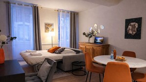 A hotel room with a bed, a desk, a dining table with chairs, a laptop, and a painting on the wall. - Grand T2 Cosy -Rouen historic center near Hôtel de Ville - L'Hauss'Rouennais (Rouen)