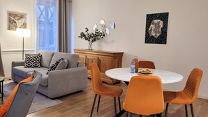 A modern living room with a grey sofa, orange chairs, a wooden cabinet, and a round dining table. - Grand T2 Cosy -Rouen historic center near Hôtel de Ville - L'Hauss'Rouennais (Rouen)
