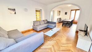 A modern living room with a grey sectional sofa, a glass coffee table, and a herringbone wooden floor.