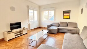 A modern living room with a flat-screen TV, a wooden coffee table, a grey sofa, and a radiator.