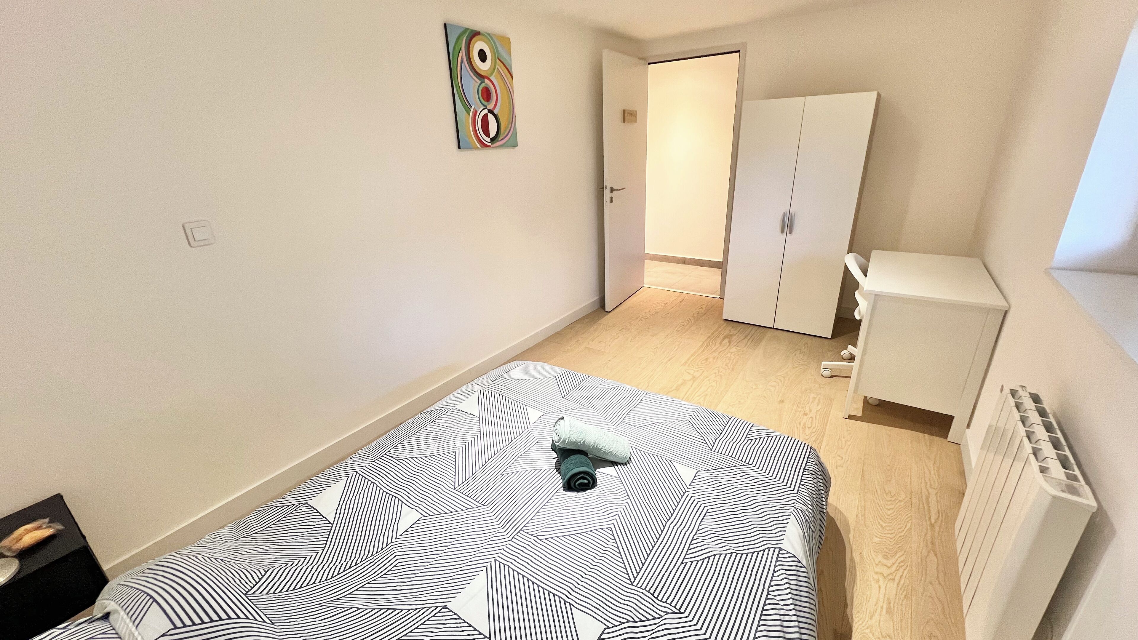 A small, neatly arranged bedroom with a bed, a wardrobe, and a radiator.
