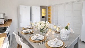 A modern kitchen with white appliances, a dining table set for six with white plates, silverware, and a centerpiece of flowers.