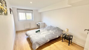 A bedroom with a bed, a desk, a radiator, and a window.