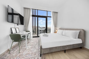 A hotel room with a bed, a desk with a chair, a TV mounted on the wall, and a large window with curtains. - Free Housekeeping Visits During Your Stay - Stayshort - Contemporary Studio Retreat in Meydan for 2 (Dubai)