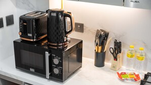 Una cucina con forno a microonde, tostapane e macchina del caffè sul piano di lavoro, oltre a un portacoltelli, forbici e bottiglie d'acqua.