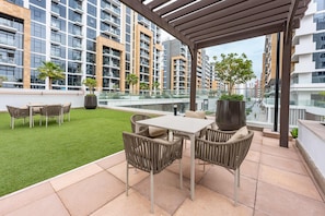 A rooftop terrace with a dining area, artificial grass, and potted plants. - Free Housekeeping Visits During Your Stay - Stayshort - Contemporary Studio Retreat in Meydan for 2 (Dubai)