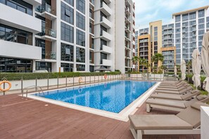 A modern apartment building with a swimming pool and lounge chairs. - Free Housekeeping Visits During Your Stay - Stayshort - Contemporary Studio Retreat in Meydan for 2 (Dubai)