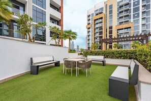 Eine Dachterrasse mit Kunstgrasanlage, einem runden Tisch mit Stühlen und einer Bank.