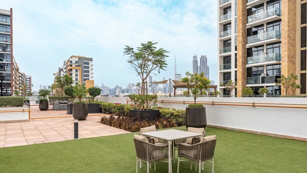 Una terrazza sul tetto con erba sintetica, un tavolo e sedie, piante in vaso e vista sullo skyline della città.