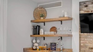 Eine kleine Küche mit weißen Schränken, Holzregalen und einem Kamin aus Stein.