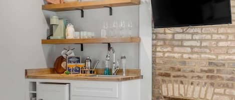 A compact kitchen with a built-in sink, wooden shelves, and a brick fireplace.
