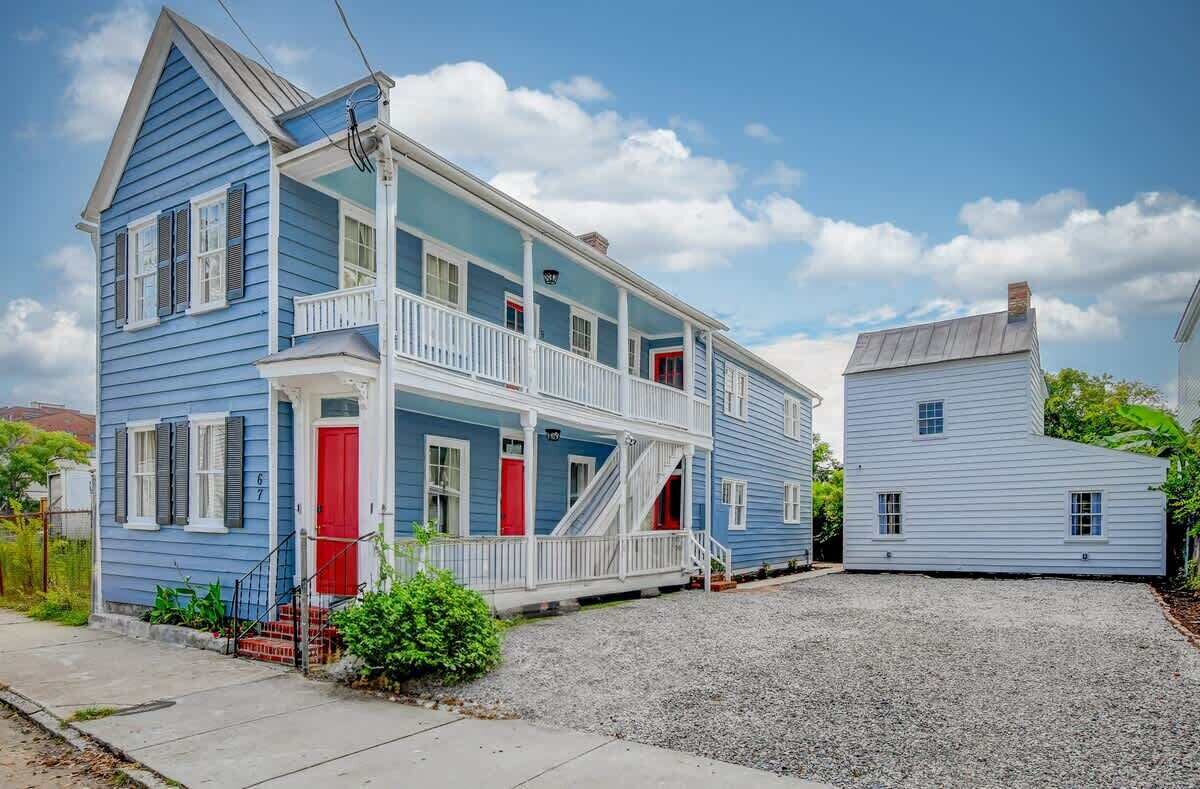 A two-story house with a porch, a red door, and a gravel driveway.