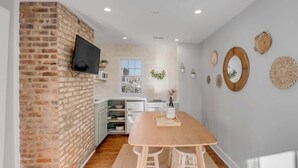 Une cuisine moderne avec un mur d’accent en briques, un téléviseur à écran plat et une grande table en bois.