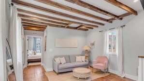 Un salon moderne avec des poutres apparentes en bois, un canapé gris, un fauteuil rose et une table basse ronde.