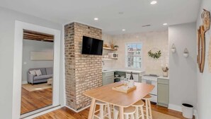Une cuisine moderne avec un mur d’accent en briques, un téléviseur à écran plat et un coin repas équipé de tabourets.