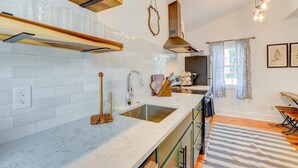 A modern kitchen with white tiles, a stainless steel sink, wooden shelves, and a hanging light fixture. - Cottage with Privacy, 150ft to King + Parking (Charleston)