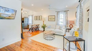 A spacious living room with hardwood flooring, a white sofa, a round coffee table, and a dining area with a table and chairs. - Cottage with Privacy, 150ft to King + Parking (Charleston)