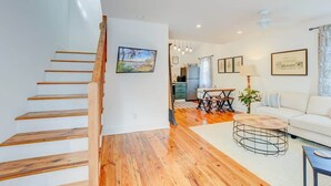 A modern apartment with a wooden staircase, a dining area with a table and chairs, a sofa, and a kitchen in the background. - Cottage with Privacy, 150ft to King + Parking (Charleston)
