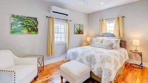 A bedroom with a bed, a chair, an air conditioning unit, and a window with curtains. - Cottage with Privacy, 150ft to King + Parking (Charleston)