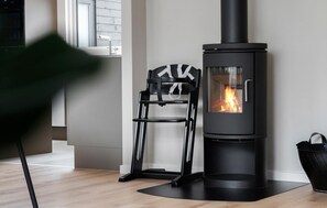 A modern kitchen with a black wood-burning stove, a black chair, and a black trash bin. - Beautiful home in Ringkøbing with sauna (Ringkøbing)